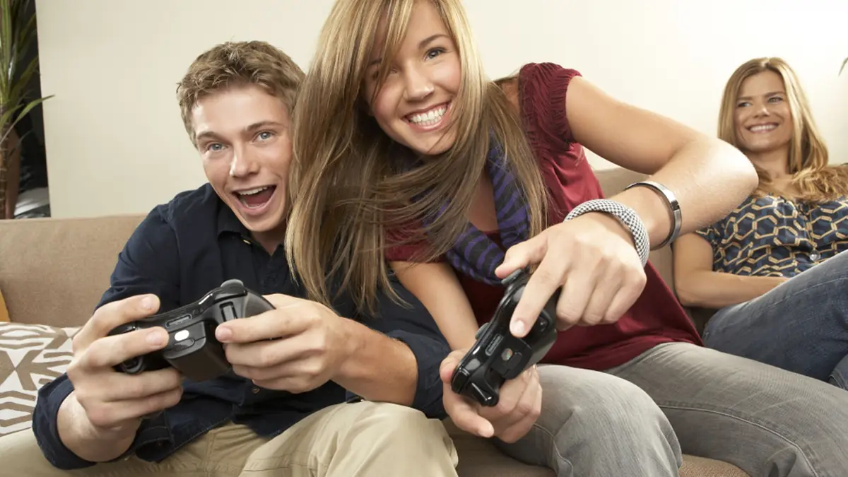 Teman-teman tertawa sambil bermain game ko-op bersama di sofa